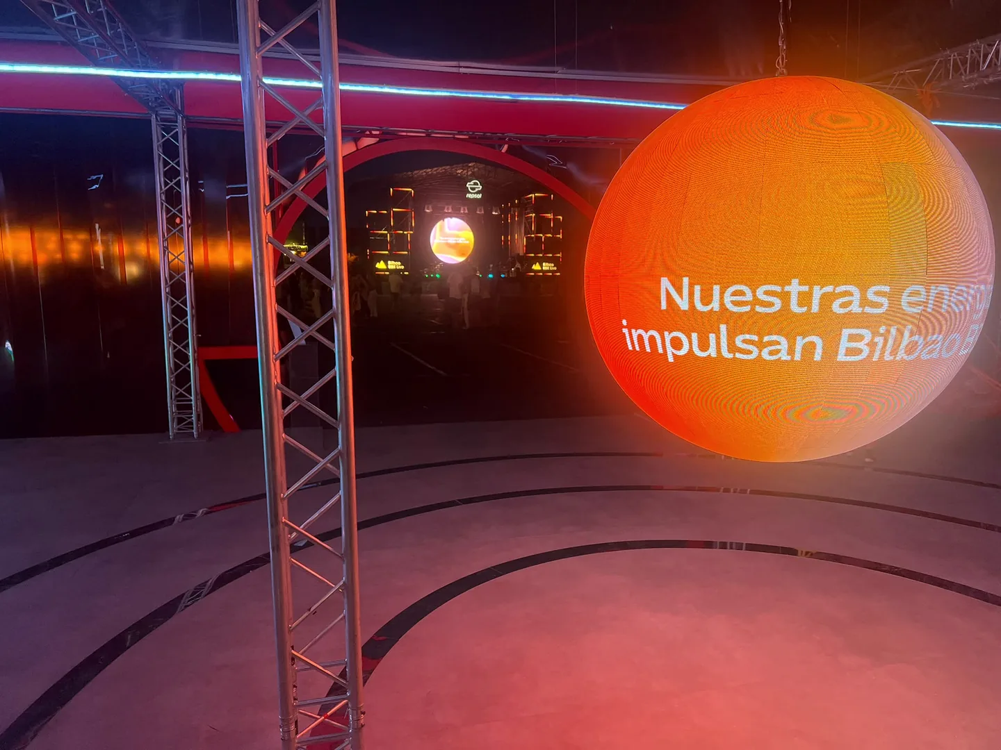 Esfera LED iluminada en naranja junto a la instalación circular del festival.